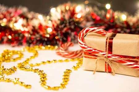 Christmas gift in a box wrapped in craft paper, tied with ribbon and rope, caramel cane. decorations with garland lights in a blur, beads, red tinsel. New year. Backgroundの写真素材