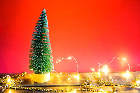 Christmas tree on a red background with lights of garlands, caramel striped cane, Santa hat, tinsel. New year, festive atmosphere. Copy spaceの写真素材