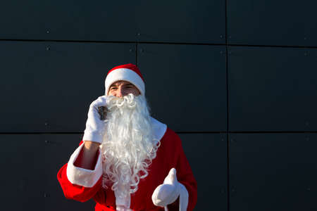 Modern Santa Claus talking on the phone. Ordering the services of an animator for the Christmas and new year. Online greetings via the Internet and mobile communication, social distanceの写真素材