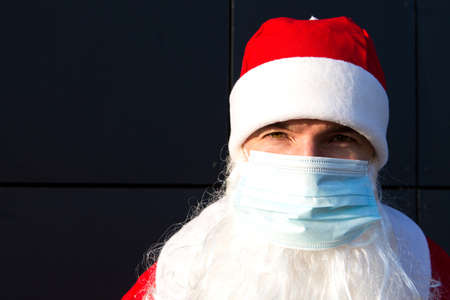Santa Claus with white beard in red coat in a medical mask. Christmas in the coronavirus pandemic, seasonal diseases, SARS and pneumonia in the holidays. Protection from viruses in the new yearの写真素材