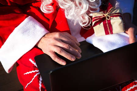 Santa Claus with a laptop and a gift in his hand. Order gifts for Christmas and new year through the online store. Booking the services of an animator for the holidays.の写真素材