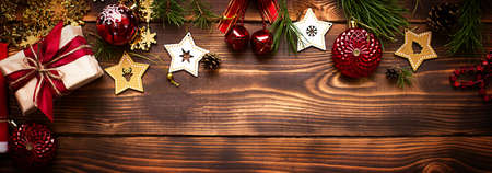 Frame with Christmas decor on a wooden background. New year, holiday atmosphere, green spruce branches, decorations: stars, gift box, beads, ball, bells, cones. Space for text, flat layの写真素材
