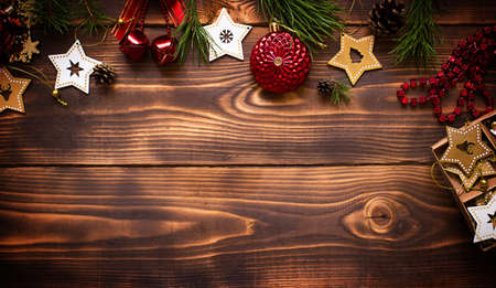 Frame with Christmas decor on a wooden background. New year, holiday atmosphere, green spruce branches, decorations: stars, gift box, beads, ball, bells, cones. Space for text, flat layの写真素材