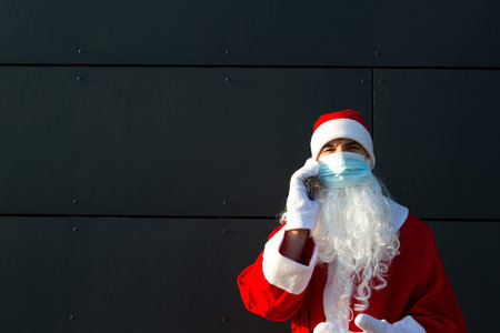 Santa Claus in a medical mask with a smartphone. Online greetings, ordering services for Christmas...