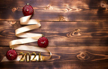 A Christmas tree made of gold ribbon with the numbers 2021 is decorated with red balloons on a dark wooden background. Flat lay. Space for text. New year, Santa hat.の写真素材