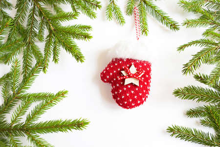 Red knitted mitten Christmas decor on a green spruce branch on a white background. Frame, copy space. Christmas new year, Christmas tree. Keep warm in winterの写真素材