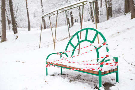 Street bench in the Park in winter in the snow is tied with a striped ribbon as a sign of prohibition of use. Restrictions, keeping the distance. Painted, can't sit, covid-19 epidemicの写真素材