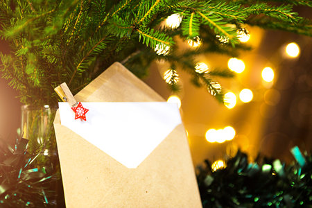 Envelope with sheet of paper- letter to Santa Claus, Copy space on a Christmas background of defocus lights in bokeh, garlands, fir branches. Clothespin-star. New year, wish list, dream, giftsの写真素材