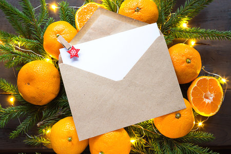 Envelope with a sheet of paper-a letter to Santa Claus, Copyspace on a Christmas background of tangerines, garlands, fir branches. Clothespin-star in place for notes. New year, wish list, dream, giftsの写真素材