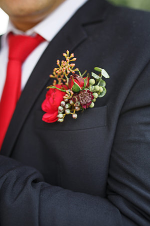 The groom's wedding boutonniere of succulents and red flowers in a black jacket with a red tie....
