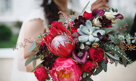 Red wedding bouquet of bride. Floristics, festive decoration of fresh flowers of the ceremony. Symbol of love, roses in pastel shades, succulents in decorative elements, wildflowers. Space for textの写真素材