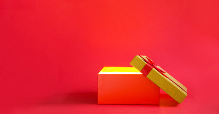 Open red gift box with a bow with a golden glow and glitter inside on a red background, banner, copyspace. universal holiday, christmas, valentine's day, new year, birthday, anniversary, presentの写真素材