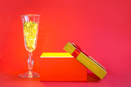 Open red gift box with golden glow and glitter inside and champagne glass with bubble beads, banner, copyspace. universal holiday, christmas, valentine's day, new year, birthday, anniversary, presentの写真素材