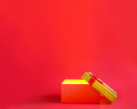 Open red gift box with a bow with a golden glow and glitter inside on a red background, banner, copyspace. universal holiday, christmas, valentine's day, new year, birthday, anniversary, presentの写真素材
