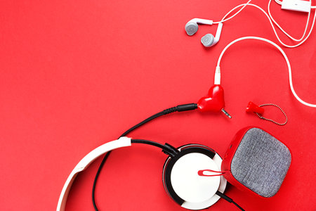 A heart-shaped headphone splitter for a couple in love. Connected to a red portable speaker and two pairs of headphones - flat lay. Valentine's day, love, modern technology, copy spaceの写真素材