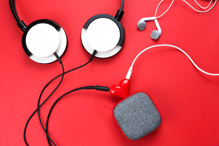 A heart-shaped headphone splitter for a couple in love. Connected to a red portable speaker and two pairs of headphones - flat lay. Valentine's day, love, modern technology, copy spaceの写真素材