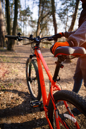 Bicycle with orange frame in the forest on the highway. A bicyclist in black and orange gloves holds the bike by the frame and seat. Theme of Cycling, sports, healthy lifestyleの写真素材