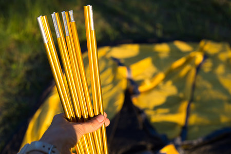 Aluminum mounting arcs for the installation of a tourist yellow tent in the hand close-up. Lightweight equipment for tourism. Outdoor activities, assembly instructions, domestic ecotourism. Copy spaceの写真素材