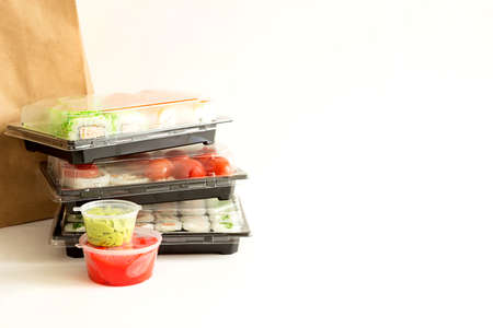 Sushi and rolls in a shipping container. Delivery of Japanese cuisine, set with maki, wasabi and ginger. Fast food to order. White background, copyspaceの写真素材