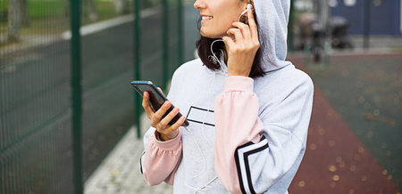 A Caucasian woman uses a smartphone via wired headphones with a headset. Phone in hand, white wire...