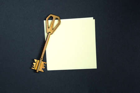 A golden key on a piece of note paper. Wish list, problem solution, idea, decoding, business concept on a black background with a square sheet. Project, rent, booking, household chores. Copy spaceの写真素材