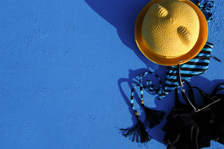 Women's accessories for a beach holiday on a blue background. The concept of a trip to the sea, relaxation, swimming, UV protection, tanning. Tourism and travel agency. Place for text. Frame. Flatlayの写真素材