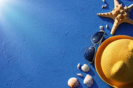 Frame with beach accessories on a nautical theme: yellow straw hat, sunglasses, starfish and shells on a blue background. Vacation concept, sea trip, UV protection, swimming. Copy space. Flatlayの写真素材