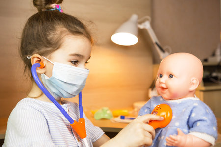 A girl with a doll plays doctor, a nurse listens to the baby through a stethoscope. Pediatrics, vaccination calendar, profession game. Medical examinationの写真素材