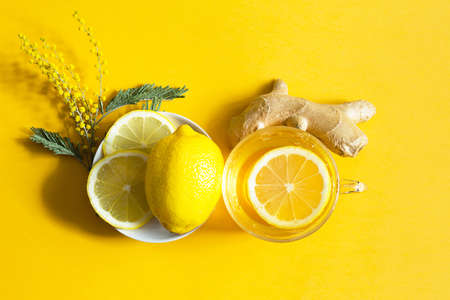 Medicinal tea in a cup, ginger, lemon, acacia-strengthen the immune system in cold season - flatly. Vitamin drink for health and ingredients on yellow background.の写真素材