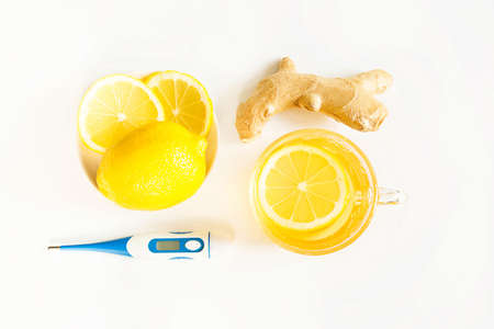Medicinal tea in cup, ginger, lemon-strengthen immune system in the cold season. Vitamin drink for health and ingredients, thermometer on a white background. Flu, cold, immunity, fever, antipyreticの写真素材