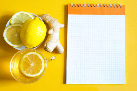 Medicinal tea in a cup, ginger, lemon-strengthen the immune system in the cold season and copy space, sheet for notes. Vitamin drink for health and ingredients on a yellow illuminating background.の写真素材