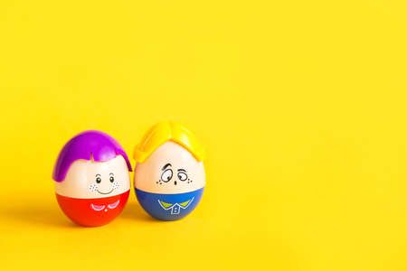 Two funny eggs boy and girl with faces on a yellow background - Easter, spring. Children's toys-a symbol of a couple of men and women, love, family. Copy spaceの写真素材