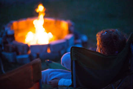 Dad and daughter sit at night by the fire in the open air in the summer in nature. Family camping tripの写真素材