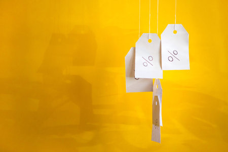 White tags with the percent sign hang on strings on a yellow background with shadows. Commerce,...