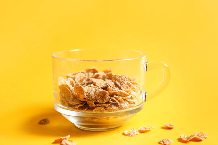 Transparent bowl with corn and multigrain flakes on a yellow background. Quick and healthy breakfast