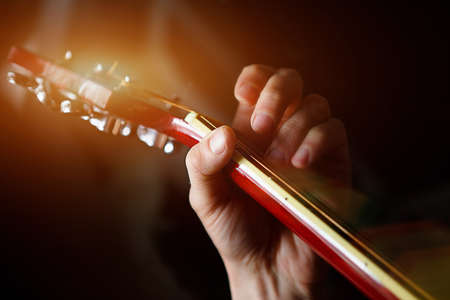 A man's hand on the fretboard of a guitar runs his fingers through the strings and clamps the chords. Instrumental music, guitar lesson on sheet musicの写真素材