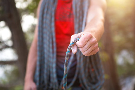 A male climber of Caucasian appearance with a coiled rope in his hand. Rope winding, knot, equipment...