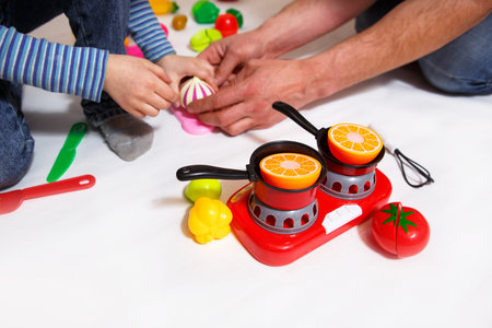 Dad and daughter play with sliced plastic vegetables and fruits with strap, cooks food on a toy...