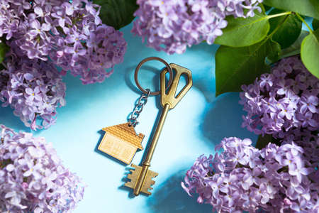 House key with keychain on blue spring background and lilac branches. Summer holiday home, booking cottage in the countryside, moving to new home, mortgage, rent and purchase real estate. Tourismの写真素材