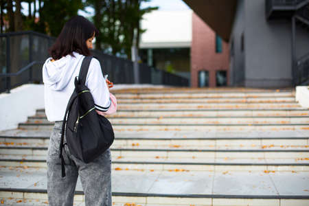 A female student with a black backpack and a notebook in her hands stands on the steps in front of the university. Higher education, the beginning of the school year, back to school. Copyspaceの写真素材