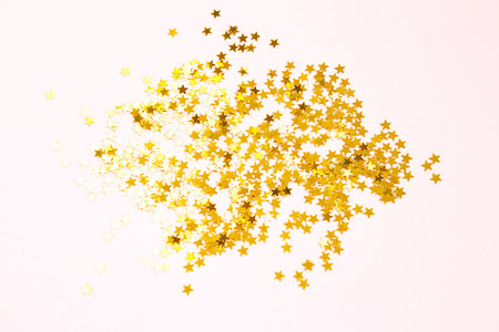 Gold sequins in the shape of stars shimmer on a pink background. Backgrounds with copyspace for a...