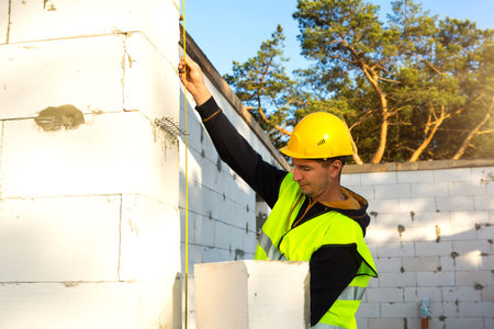 Construction worker at construction site measures the length of the window opening and the wall with...