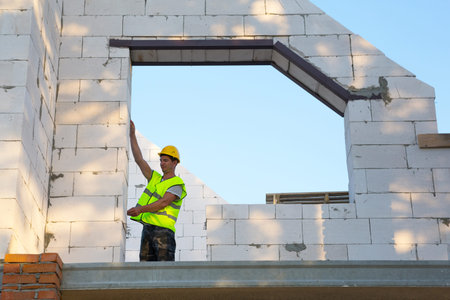 Construction worker at construction site measures the length of the window opening and the wall with...