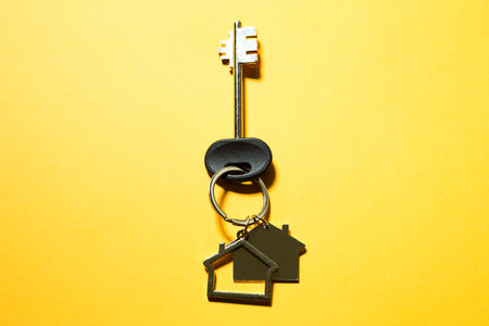 Key chain in the shape of wooden house with key on a yellow background. Building, design, project,...