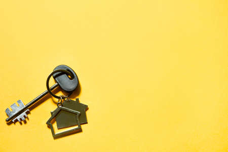 Key chain in the shape of wooden house with key on a yellow background. Building, design, project, moving to new home, mortgage, rent and purchase real estate. Copy spaceの写真素材
