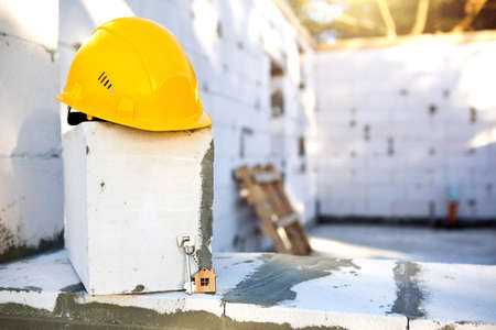 Construction yellow hardhat and key to house on window of housing made of blocks of porous concrete. Turnkey construction, future home, engineering, building. Work safety. Copy spaceの写真素材