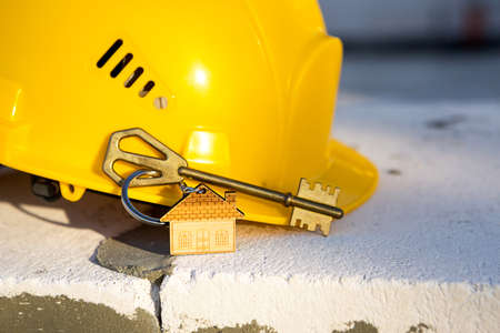Construction yellow hardhat and key to house on window of housing made of blocks of porous concrete. Turnkey construction, future home, engineering, building. Work safety. Copy spaceの写真素材