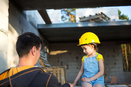 Dad and daughter are at construction site of their future home. The choice of the future profession of a builder is inherited by child. The expectation of moving, the dream of a house. Mortgage, loanの写真素材