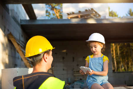 Dad and daughter are at construction site of their future home. The choice of the future profession of a builder is inherited by child. The expectation of moving, the dream of a house. Mortgage, loanの写真素材