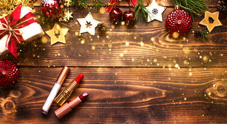 Red lipstick and lip gloss and eyelids on a wooden background in the Christmas decor. Holiday makeup for the new year, gift, shopping, women's desires. Space for text, flat layの写真素材